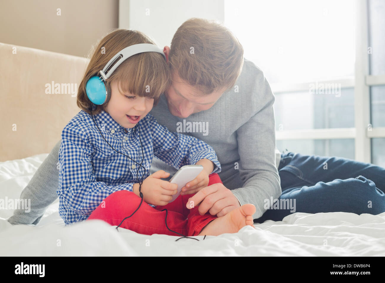 Metà padre adulto con ragazzo ascoltando musica sulle cuffie in camera da letto Foto Stock