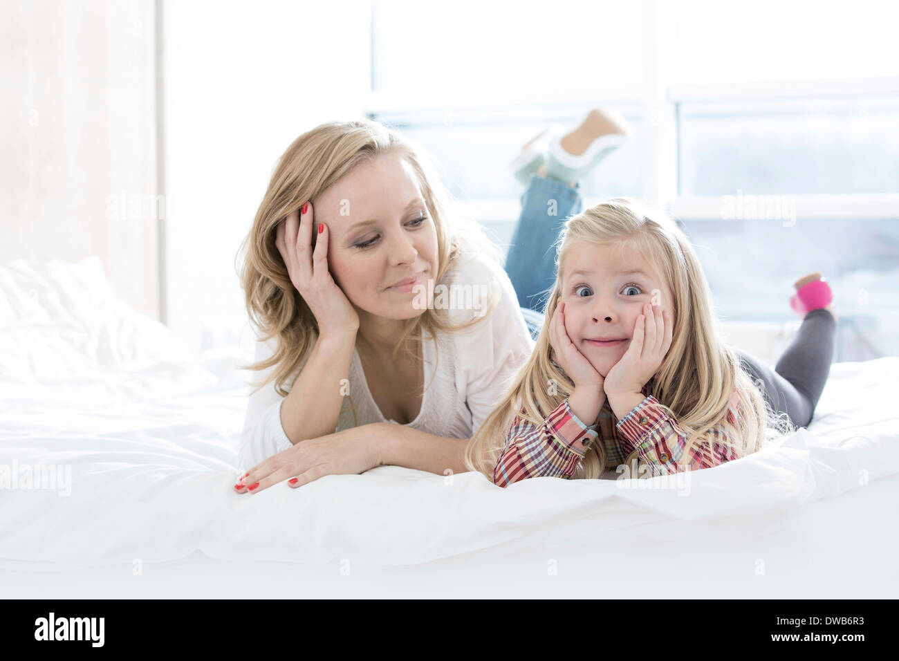 Madre guardando carino figlia rendendo volti mentre giaceva a letto Foto Stock