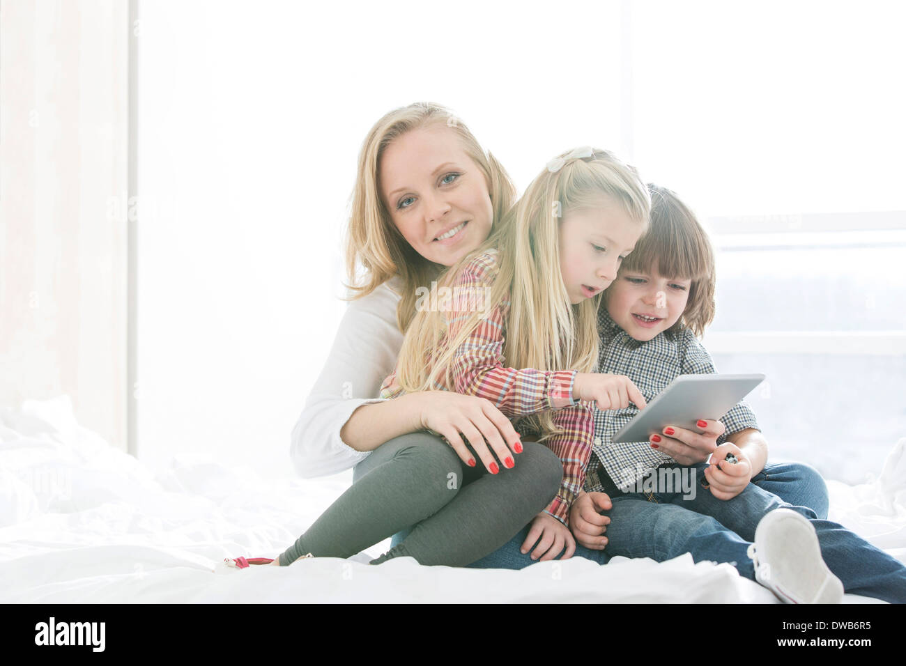 Ritratto di felice madre con i bambini utilizzando digitale compressa nella camera da letto Foto Stock