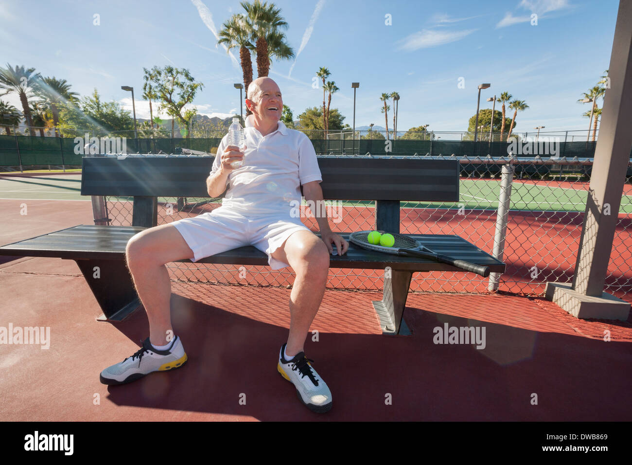 Felice senior tennista con acqua in bottiglia seduta sul banco a corte Foto Stock