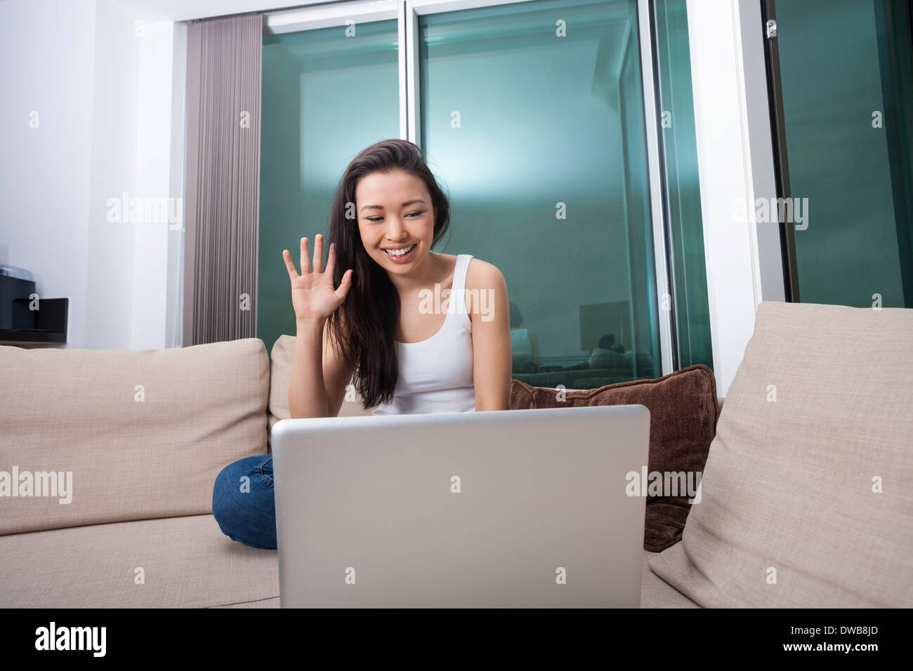 Sorridente giovane donna sventolando nella parte anteriore del computer portatile sul divano Foto Stock