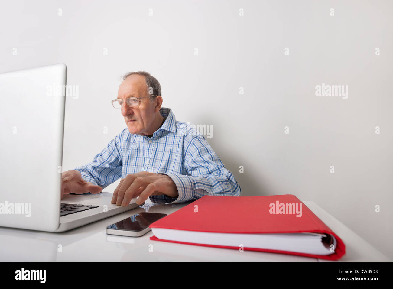 Imprenditore Senior utilizzando laptop con book binder e telefono cellulare sulla scrivania in ufficio Foto Stock