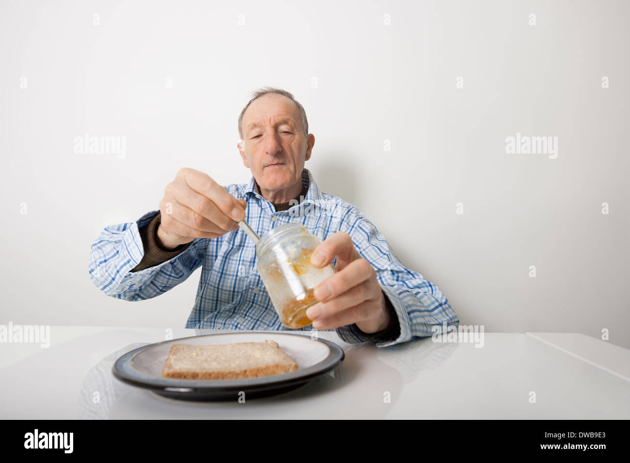 Senior uomo preparare fetta di pane e marmellata a tavola Foto Stock