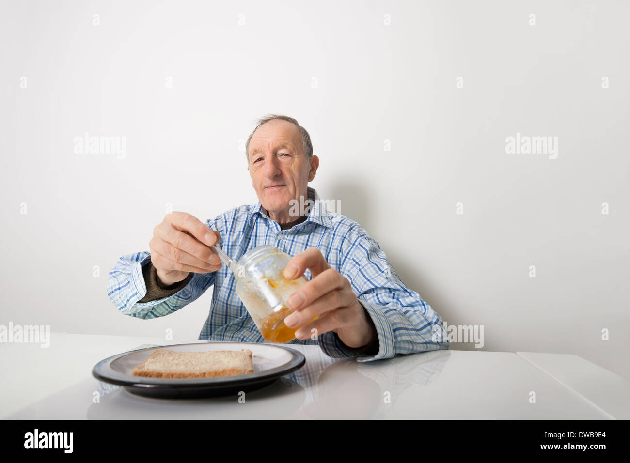 Ritratto di uomo anziano preparare fetta di pane e marmellata a tavola Foto Stock