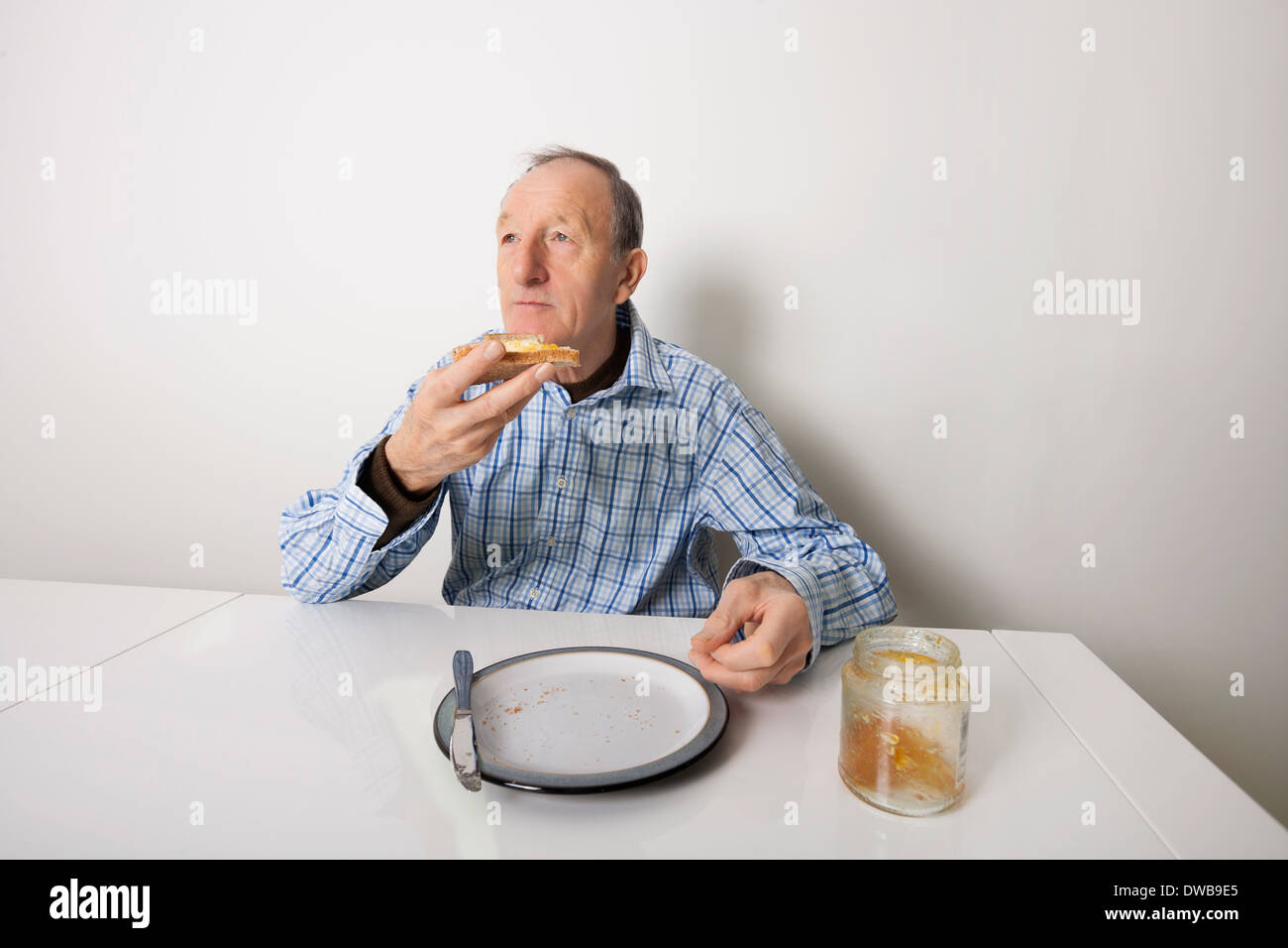 Senior uomo mangia pane spalmato con dolce Marmellata gelatinosa a tavola Foto Stock