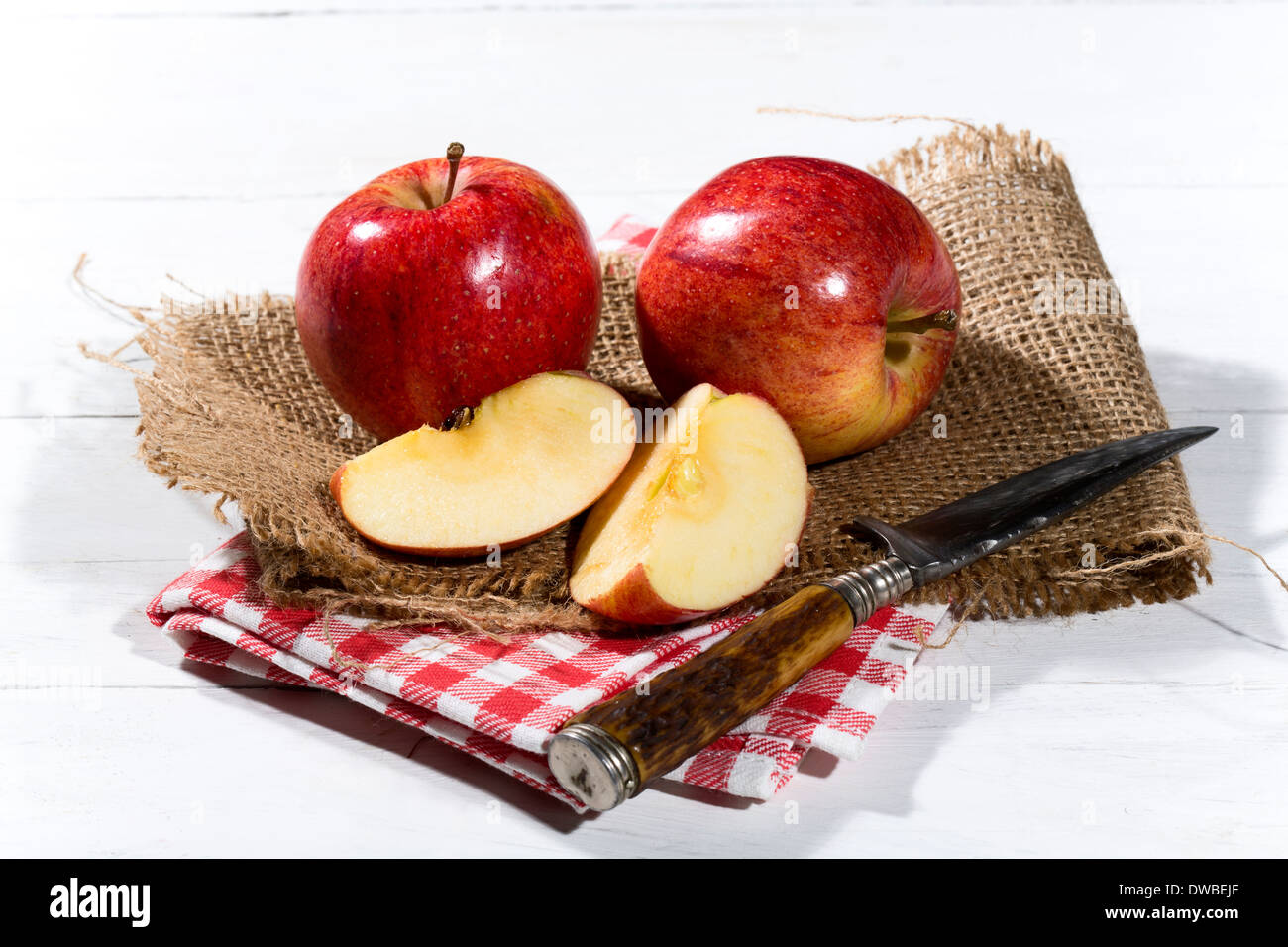 Affettato e tutta le mele rosse e un coltello sulla iuta e panno assorbente e tavolo in legno Foto Stock