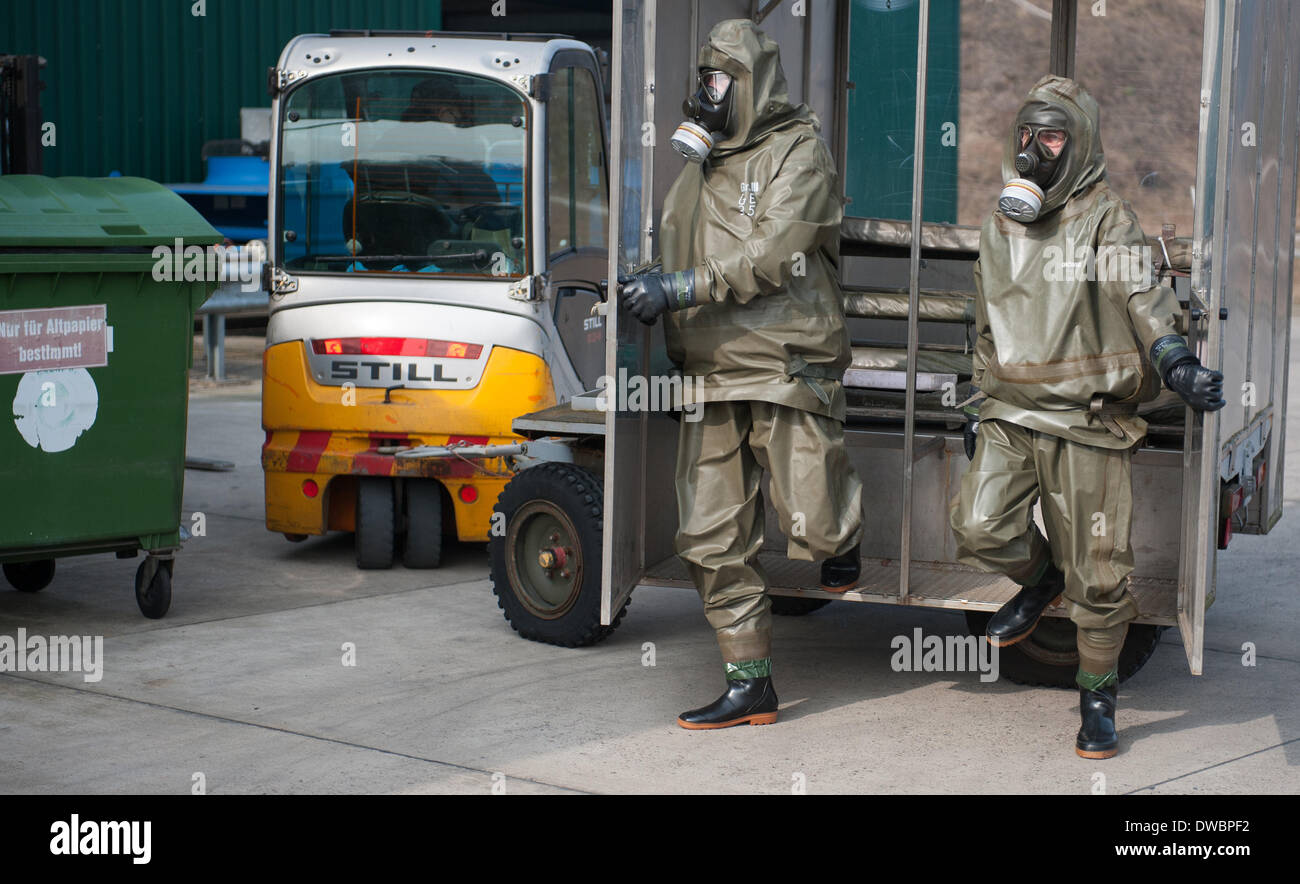 Munster, Germania. 5 Mar 2014. Due dipendenti di GEKA, la proprietà del governo azienda specializzata nello smaltimento delle armi chimiche, indossare tute di protezione come fanno un passo al di fuori di un particolare veicolo di trasporto nei locali dell'azienda in Munster, Germania, 5 marzo 2014. La GEKA (Gesellschaft zur Entsorgung von chemischen Kampfstoffen und Ruestungsaltlasten/GEKA) è la sola azienda in Germania che è coinvolto nello smaltimento delle armi chimiche da parte della Siria. Foto: Philipp Schulze/dpa/Alamy Live News Foto Stock