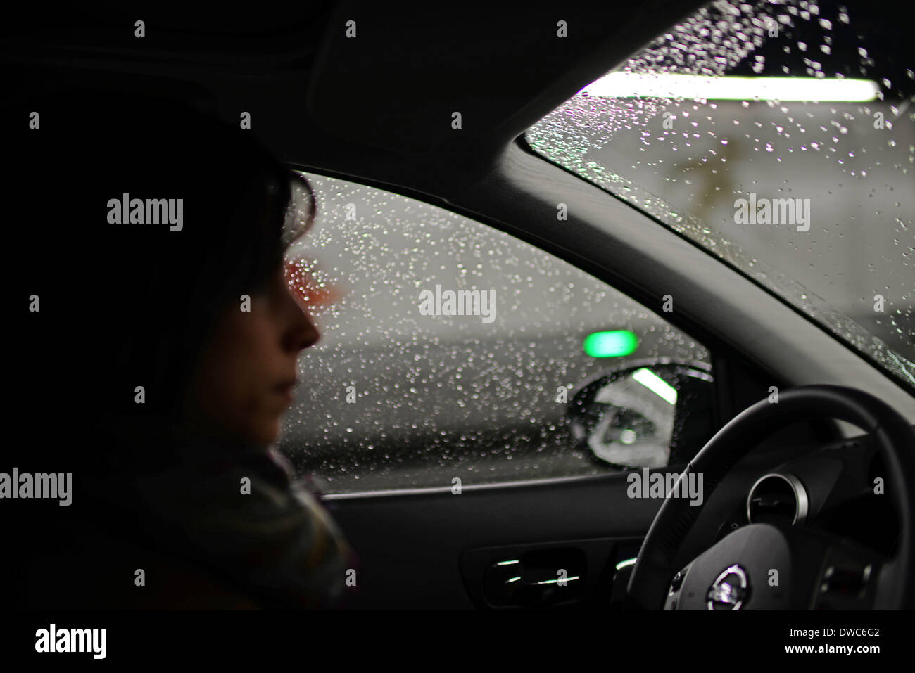 Giovane donna alla guida di auto in giorno di pioggia Foto Stock