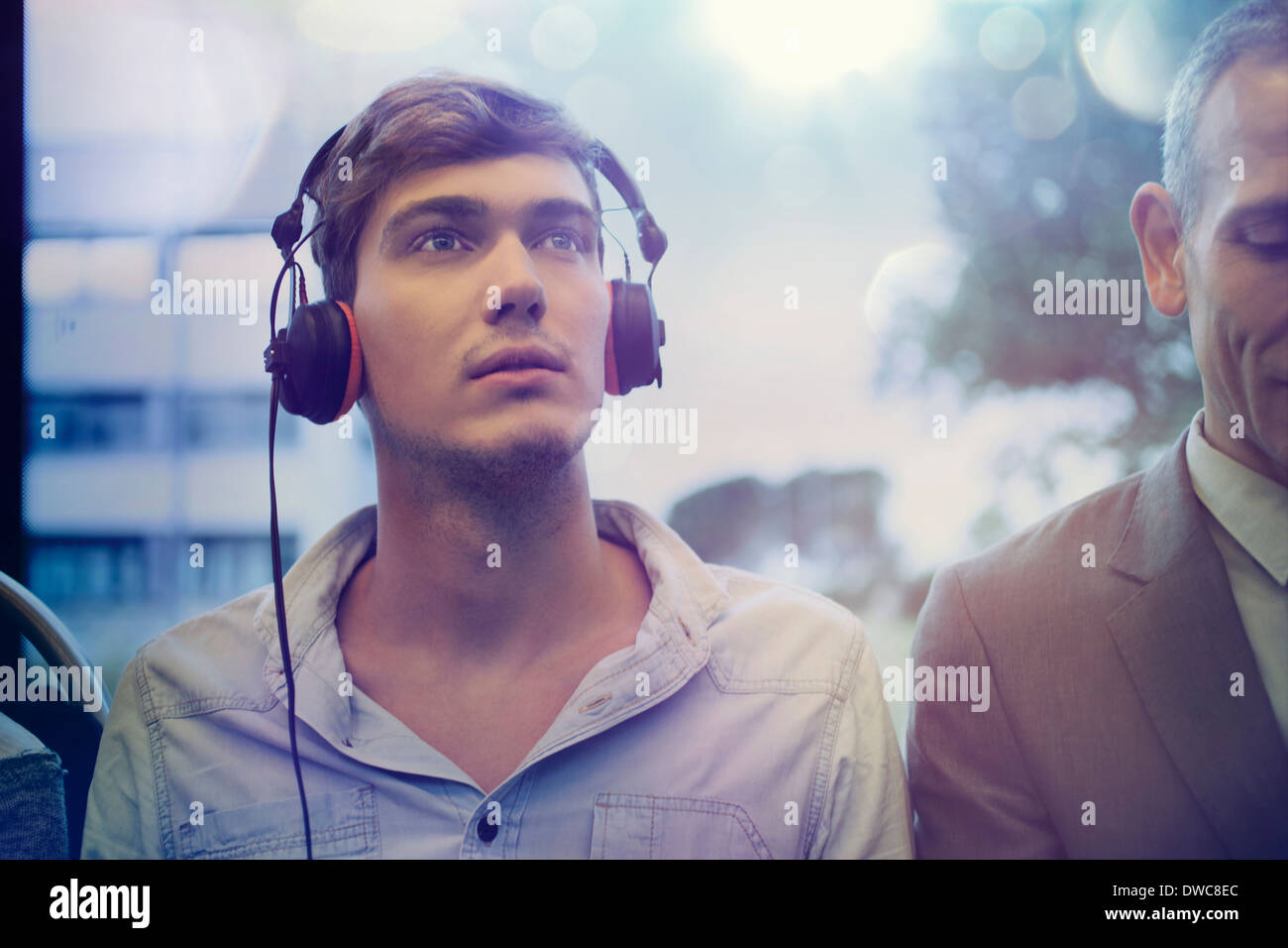 Giovane uomo fantasticando e di ascolto delle cuffie sul treno Foto Stock