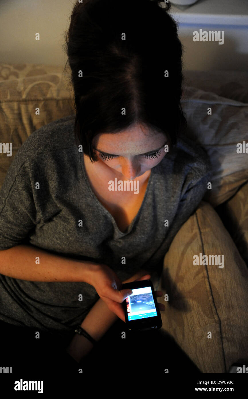 Giovane donna 20s da soli a casa utilizzando il suo telefono cellulare Foto Stock