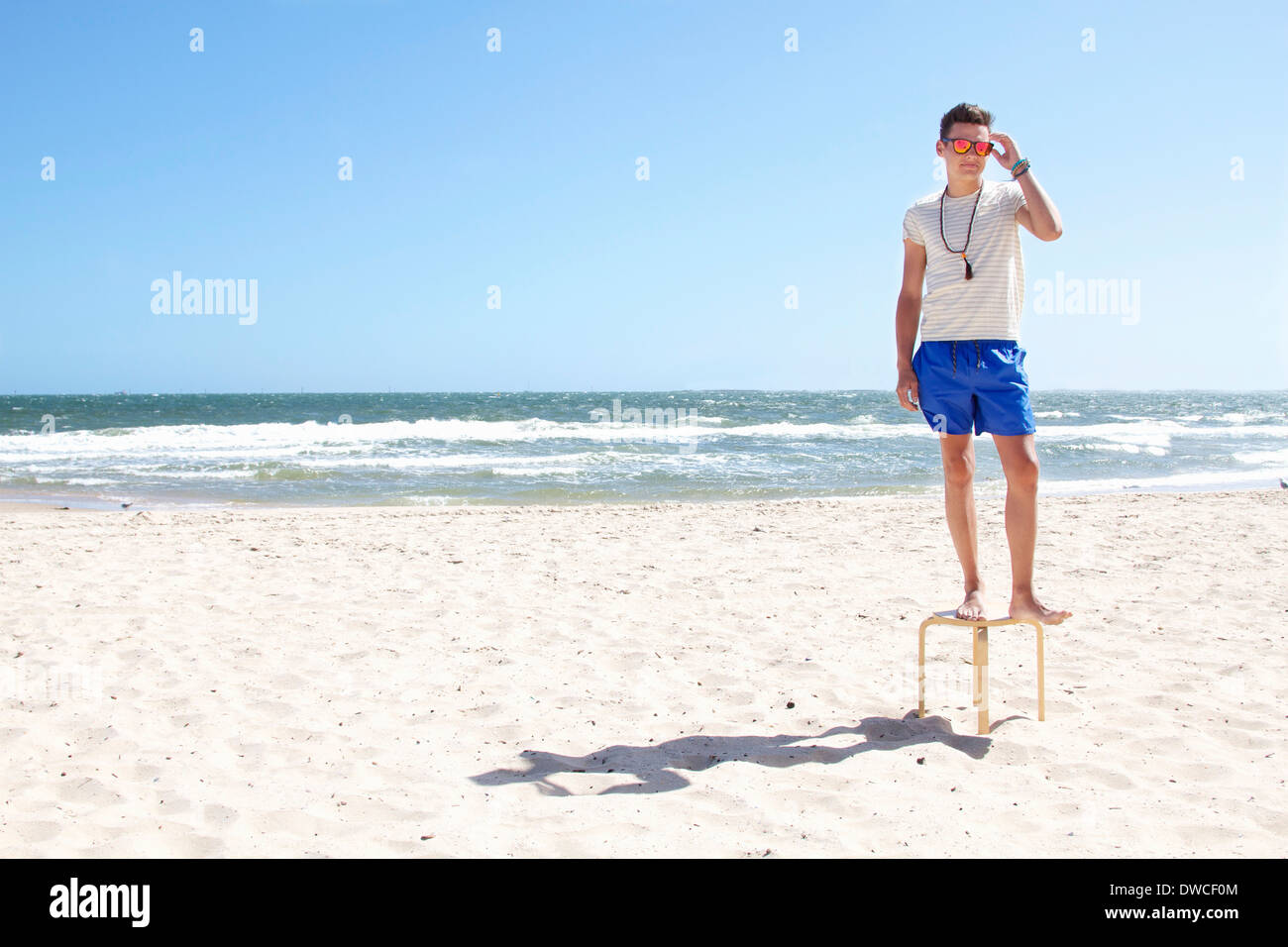 Giovane uomo che pongono sulla sommità di uno sgabello sulla spiaggia, il Port Melbourne, Melbourne, Australia Foto Stock