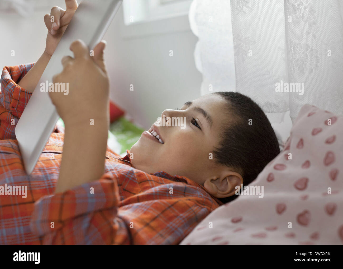 Ragazzo con tavoletta digitale mentre giaceva a letto Foto Stock