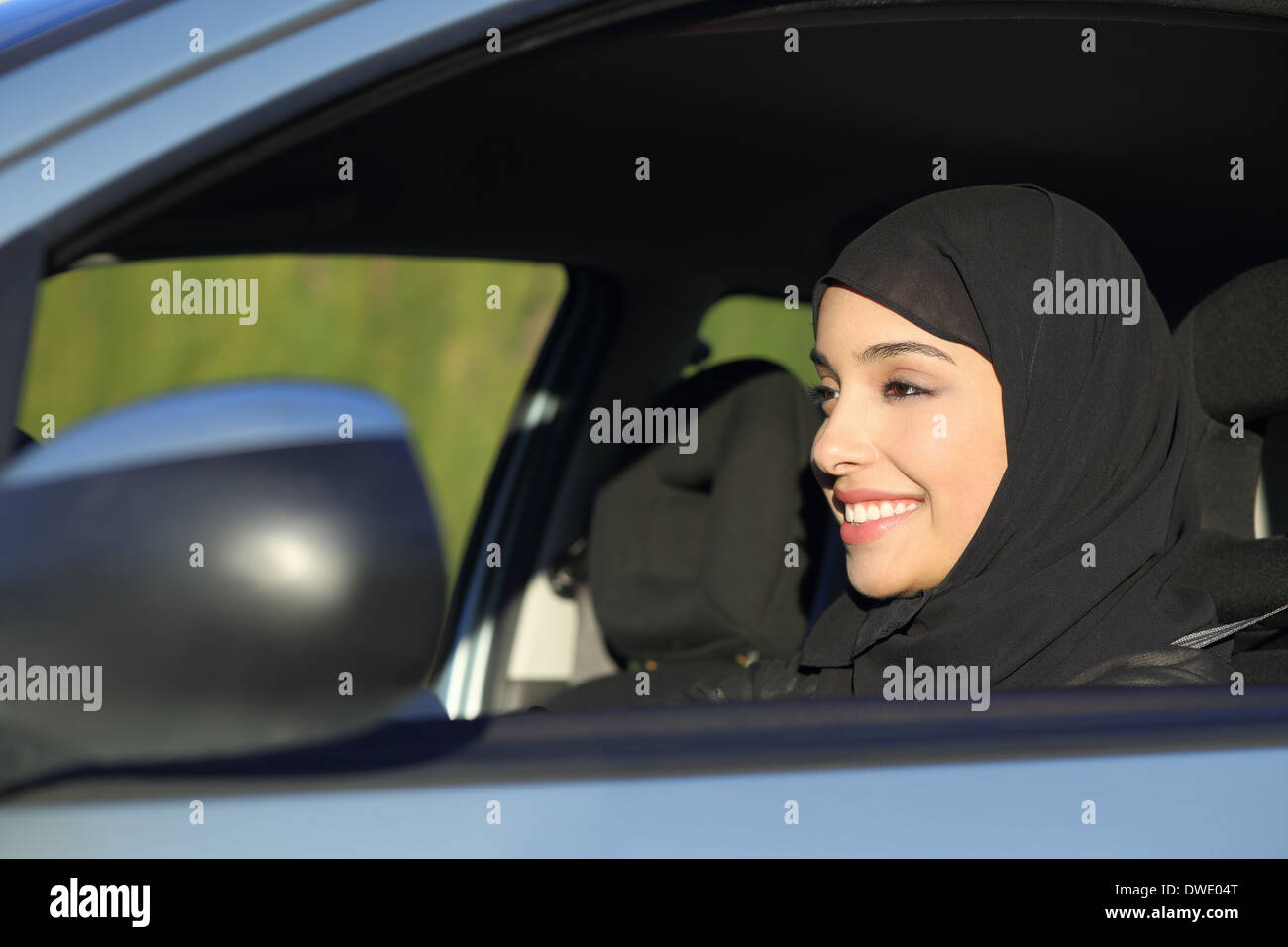 Felice arab arabia donna alla guida di una vettura sorridente con un velo Foto Stock