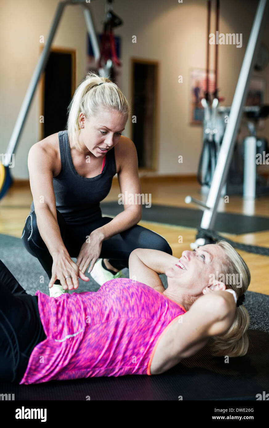 Femmina assiste istruttore senior donna nel fare sit ups in palestra Foto Stock