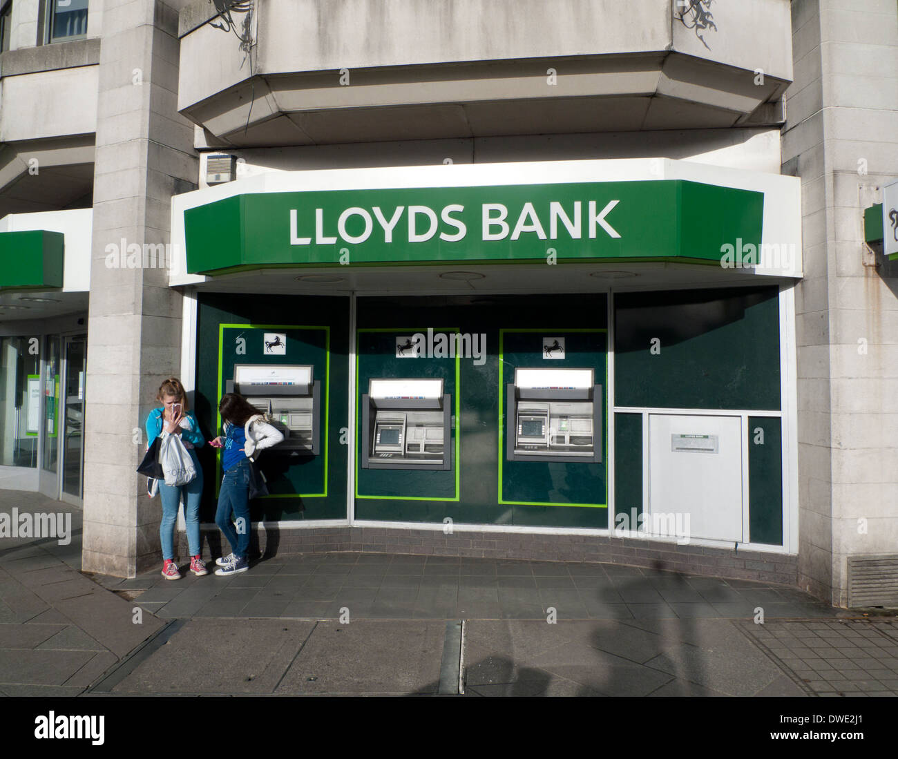 Due ragazze adolescenti scrivere messaggi su telefoni cellulari al di fuori di Lloyds Bank ATM Bancomat nel centro di Cardiff Wales UK KATHY DEWITT Foto Stock