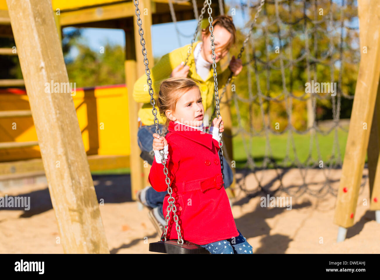 Famiglia con mamma e figlia basculante e giocare su area giochi o corte Foto Stock