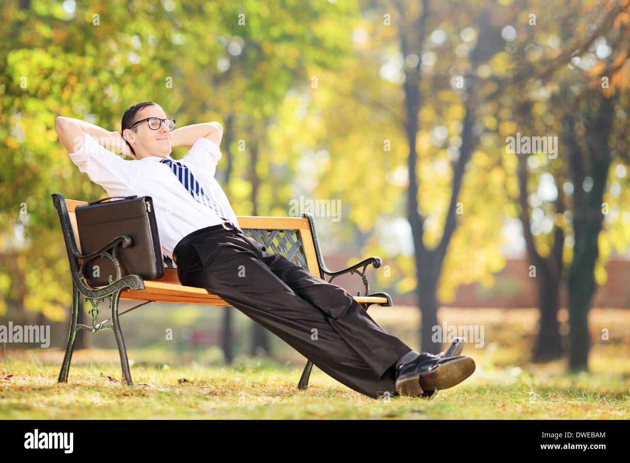 Giovane imprenditore prendendo una pausa dopo il lavoro seduto su una panchina nel parco Foto Stock