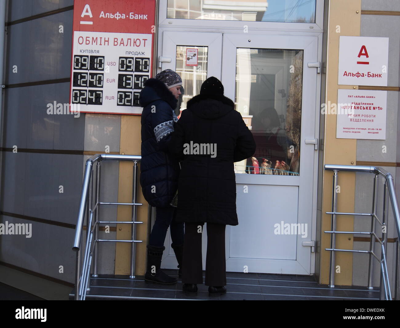 Lugansk, Ucraina. Il 6 marzo 2014. Due ragazze sono sull' orlo della Banca Alfa, a sinistra indica il quadro di valutazione valuta i prezzi. Oggi il dollaro vale 9,70 grivna, pochi giorni fa il suo prezzo superato 11.00 grivna Credit: Igor Golovnov/Alamy Live News Foto Stock