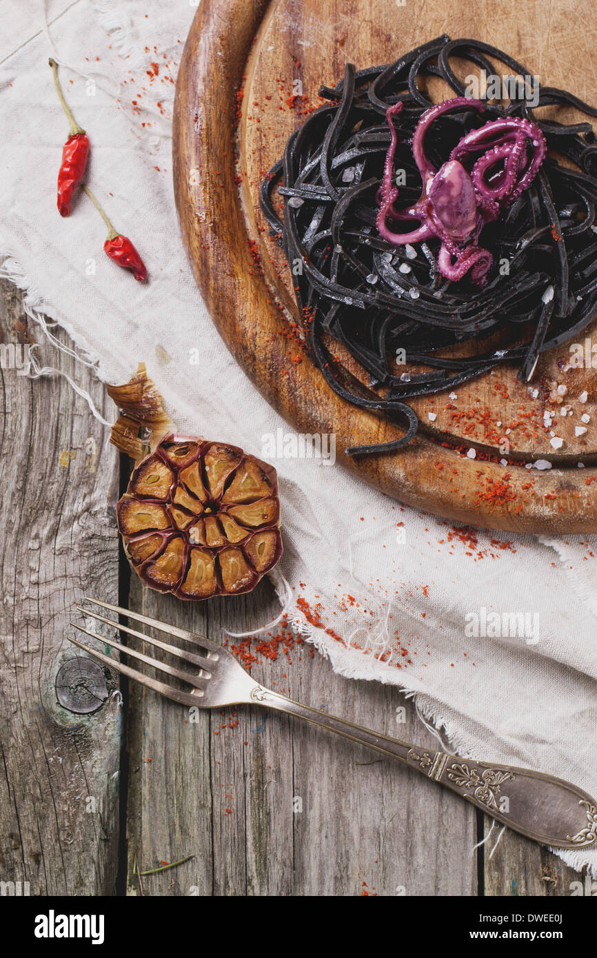 Spaghetti al nero (la pasta con il nero di seppia) con il polipo marinato e aglio grigliato servito sul tagliere di legno. Foto Stock