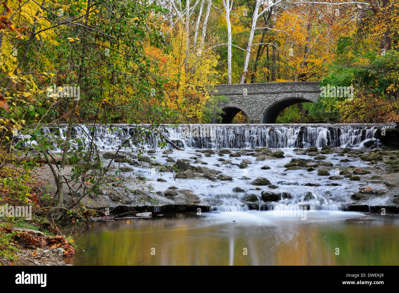 Un ponte di pietra e cascata durante l'Autunno nel parco, Sharon boschi, Southwestern Ohio, Stati Uniti d'America Foto Stock