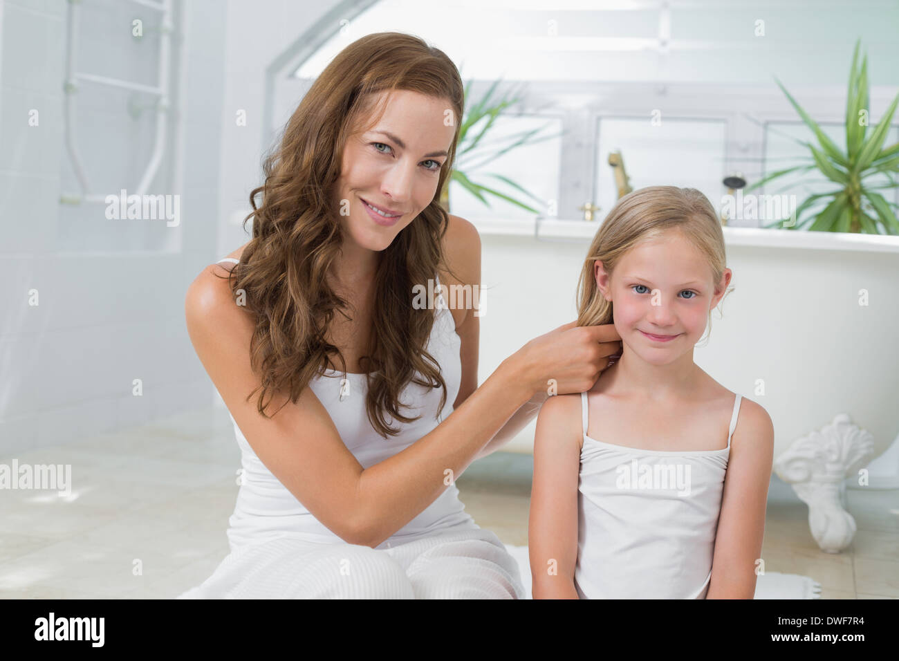 Donna sorridente trecciatura carino piccolo ai capelli della ragazza nella stanza da bagno Foto Stock
