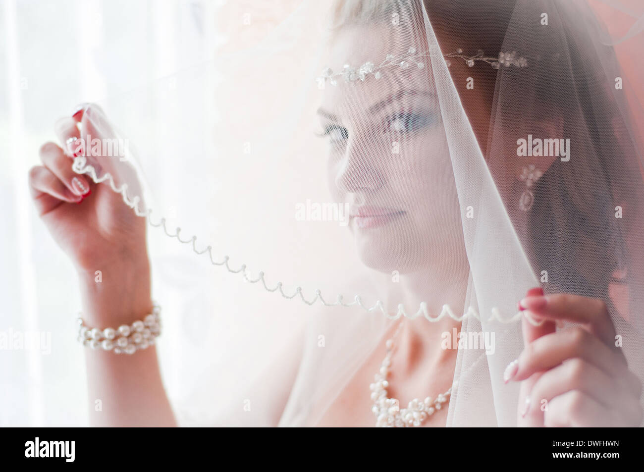 La giovane e bella sposa con un velo su una faccia in una finestra Foto Stock