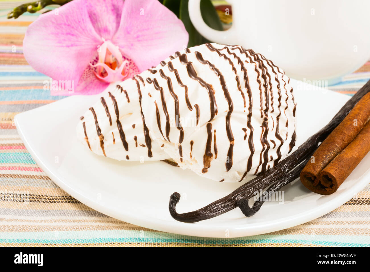Striped marshmallow su un piattino con una cannella, il baccello di vaniglia con una tazza di tè e un fiore Foto Stock