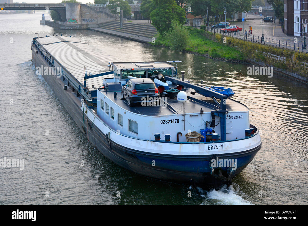 Maastricht River Meuse (Maas)i membri dell'equipaggio trasportano un'auto da carico su una grande chiatta a motore che si muove lungo una strada urbana lungo il fiume Foto Stock