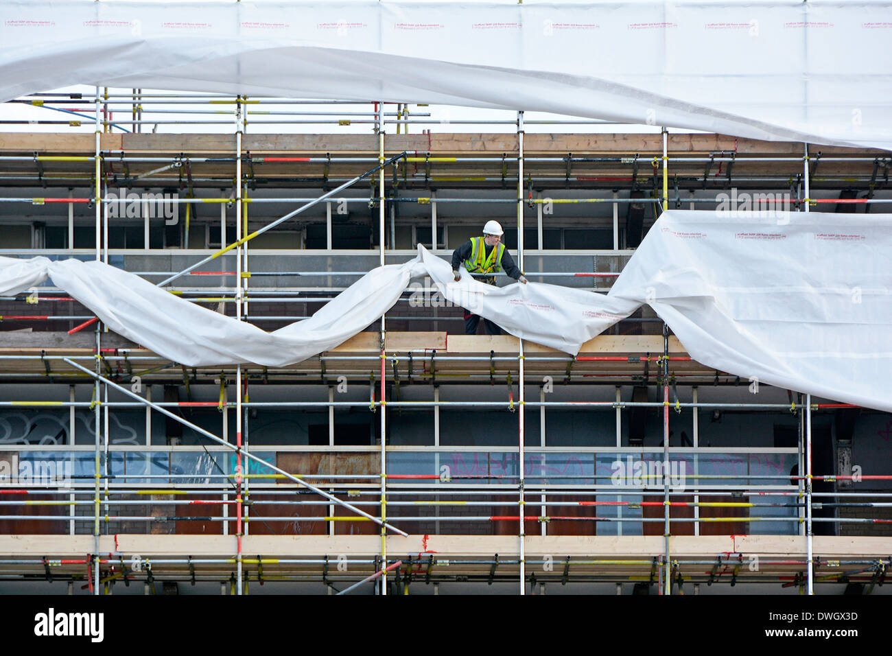 Workman in plastica di fissaggio telone cocoon al ponteggio eretto intorno all alto blocco alloggiamento prima di demolizione Southwark Sud Londra Inghilterra REGNO UNITO Foto Stock