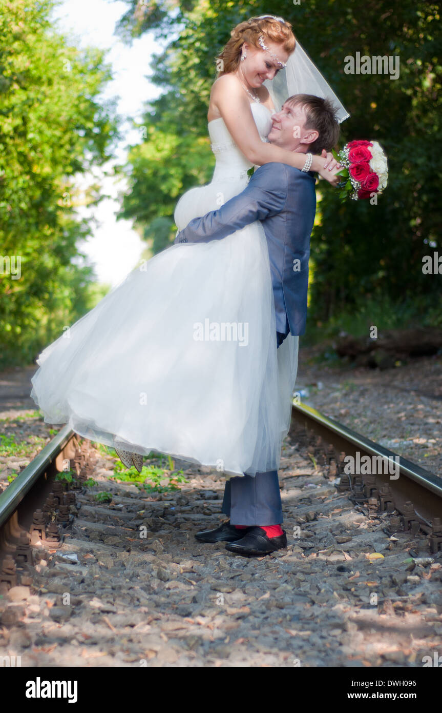 Happy sposi novelli frolic su ferrovia in estate, lo sposo sollevò la sposa su mani in alto Foto Stock