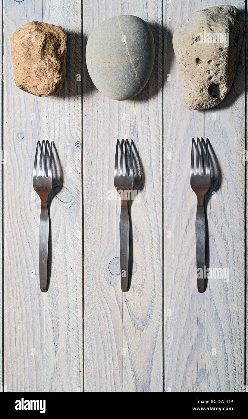 Tre Forchette e tre pietre su di un tavolo di legno. Allegoria della fame Foto Stock