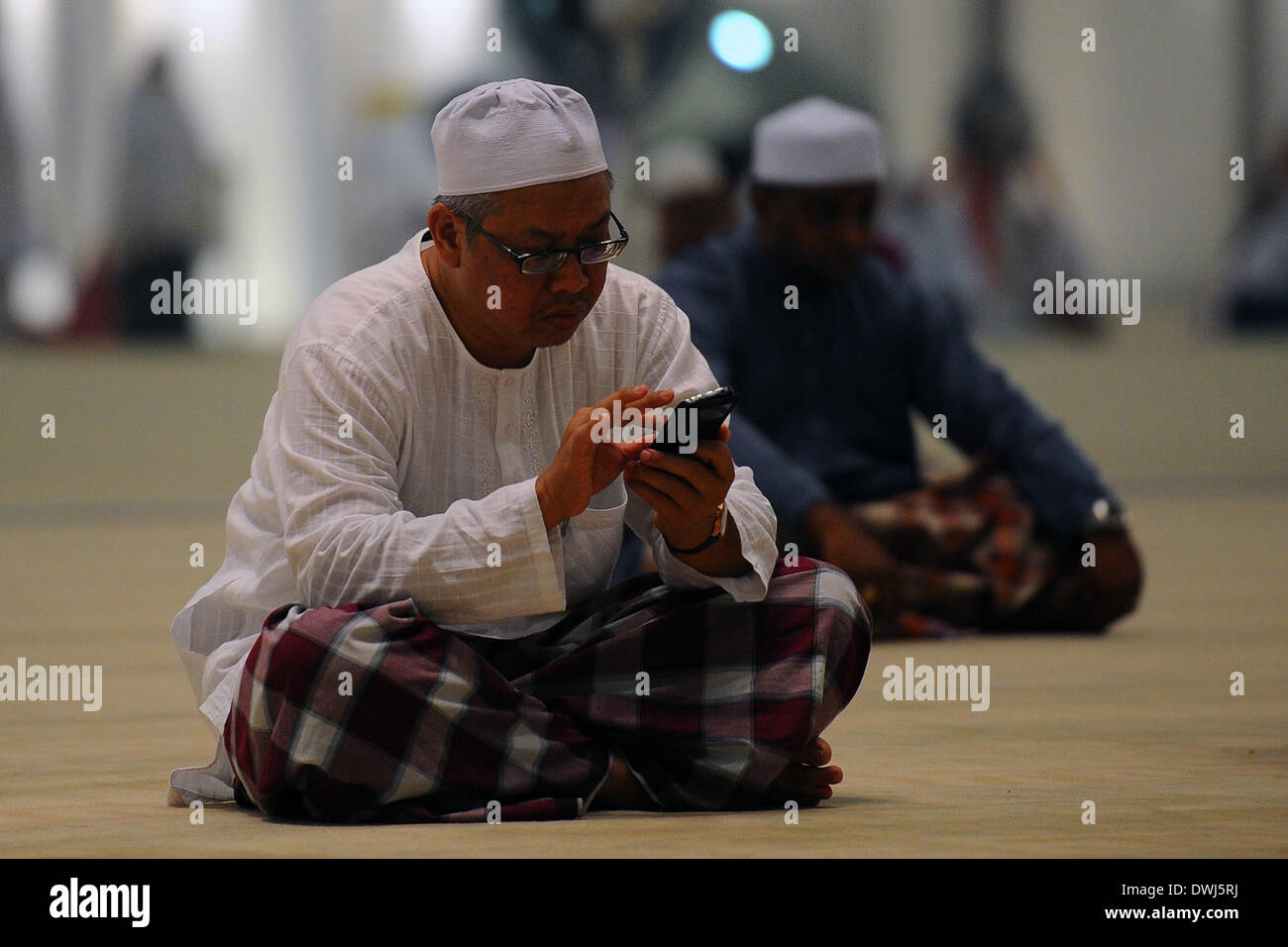 Putrajaya, Malaysia. 9 Mar 2014. Un musulmano malese uomo a controllare il suo telefono cellulare per gli aggiornamenti in una moschea durante la messa di raduno di preghiera per la Malaysia Airlines piano mancante, MH370 in Putrjaya, al di fuori di Kuala Lumpur, Malesia, Sabato, 9 marzo 2014. Radar militari indica che manca il Boeing 777 getto di Malaysia Airlines può avere ruotato indietro, Malaysia Air force chief detto Domenica decine e decine di navi e di aeromobili di tutta l'Asia riprende una battuta di caccia per il piano e la sua 239 passeggeri. Credito: Joshua Paul/NurPhoto/ZUMAPRESS.com/Alamy Live News Foto Stock