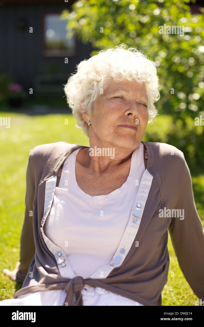 Senior donna seduta sul prato con gli occhi chiusi godendo di aria fresca- all'aperto Foto Stock