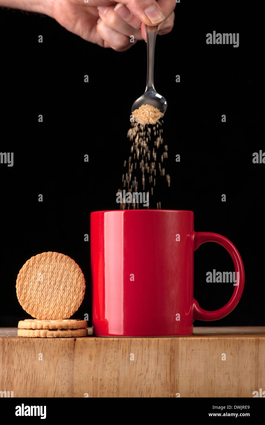 Aggiunta di zucchero per una tazza di tè o caffè Foto Stock