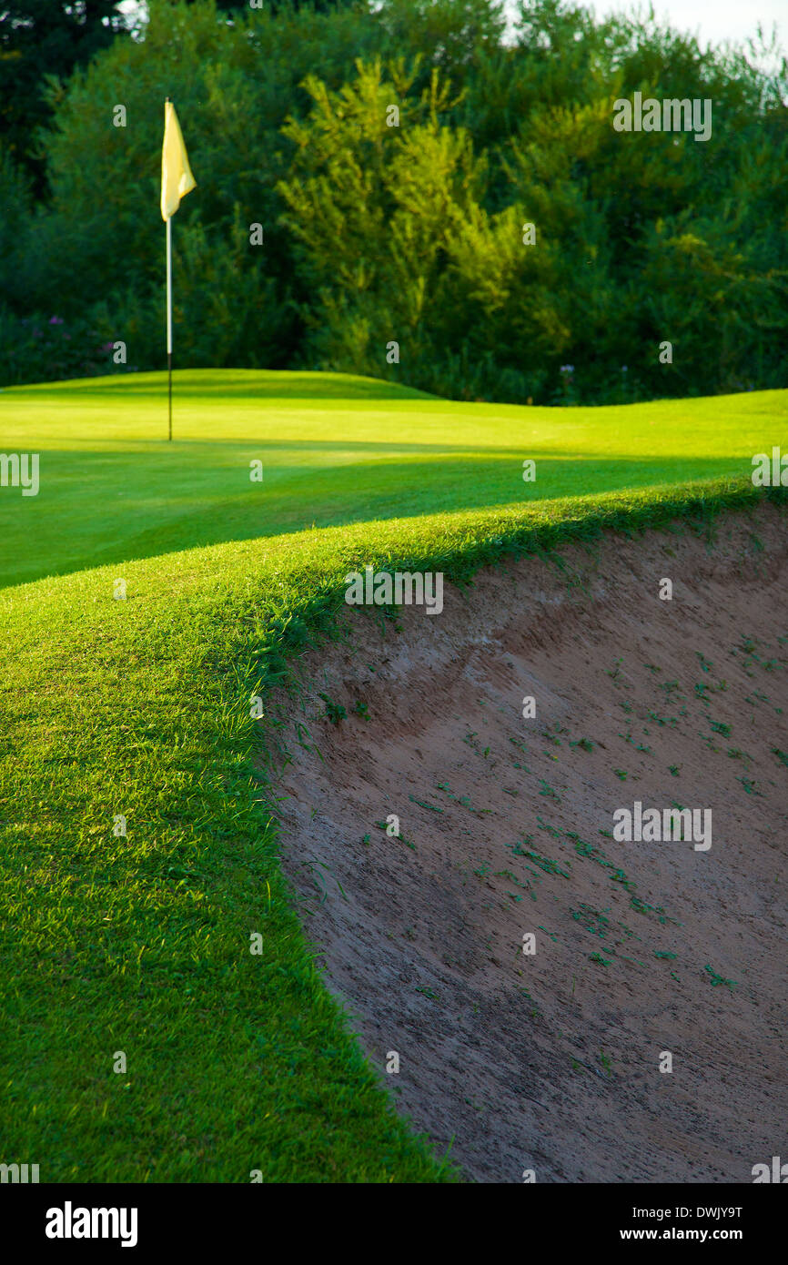 Bordo del bunker e Golf il flag nel foro sul verde su un campo da golf. Foto Stock