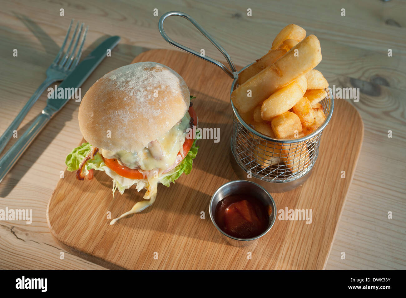 Beefburger con il formaggio e la pancetta con un ordine di fritti o scaglie di patate e un piccolo servizio di tomato ketchup. Foto Stock