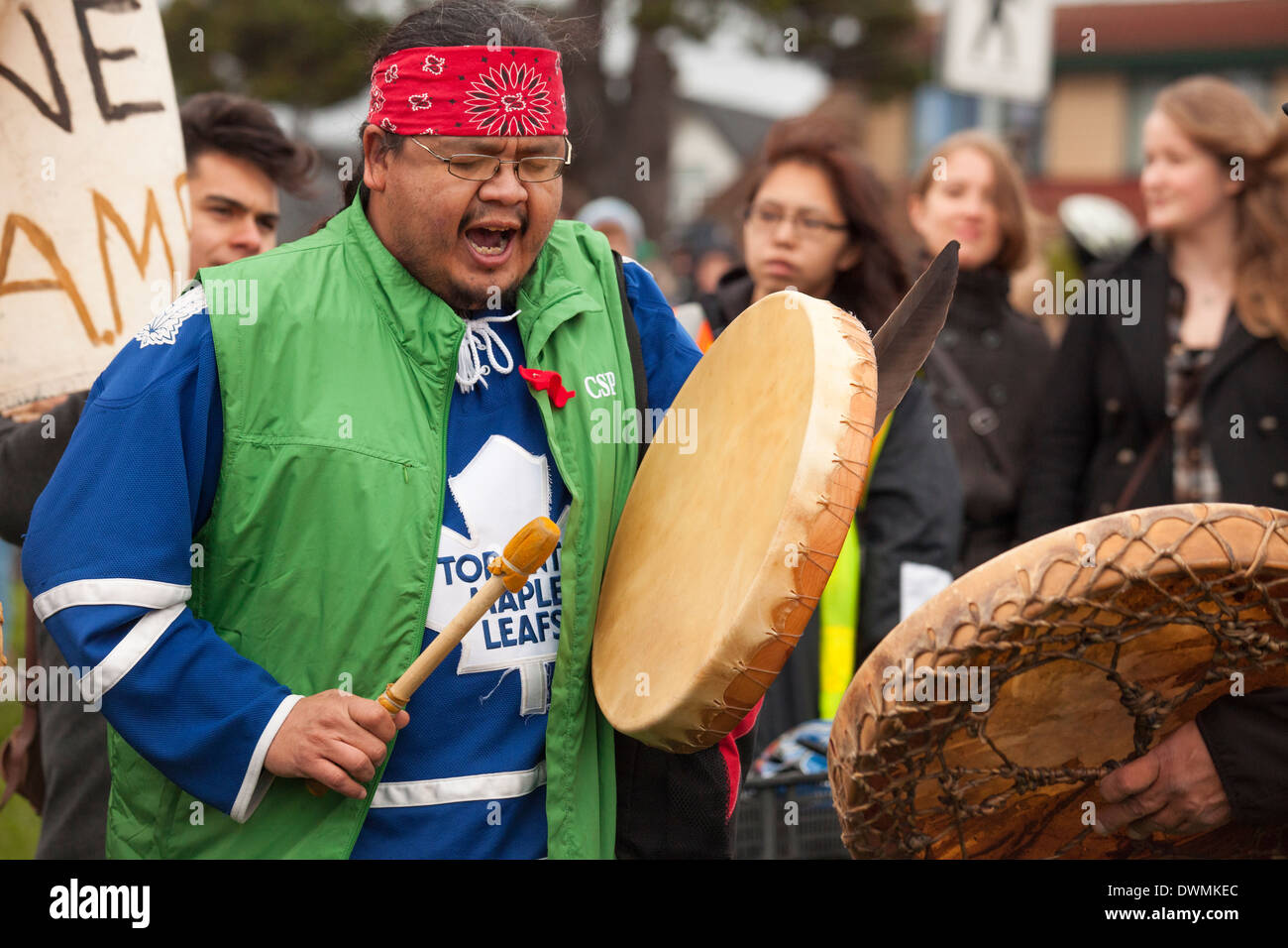 Più in anticipo le prime nazioni uomo battendo il tamburo con manifestanti a Anti oleodotto rally-Victoria, British Columbia, Canada. Foto Stock