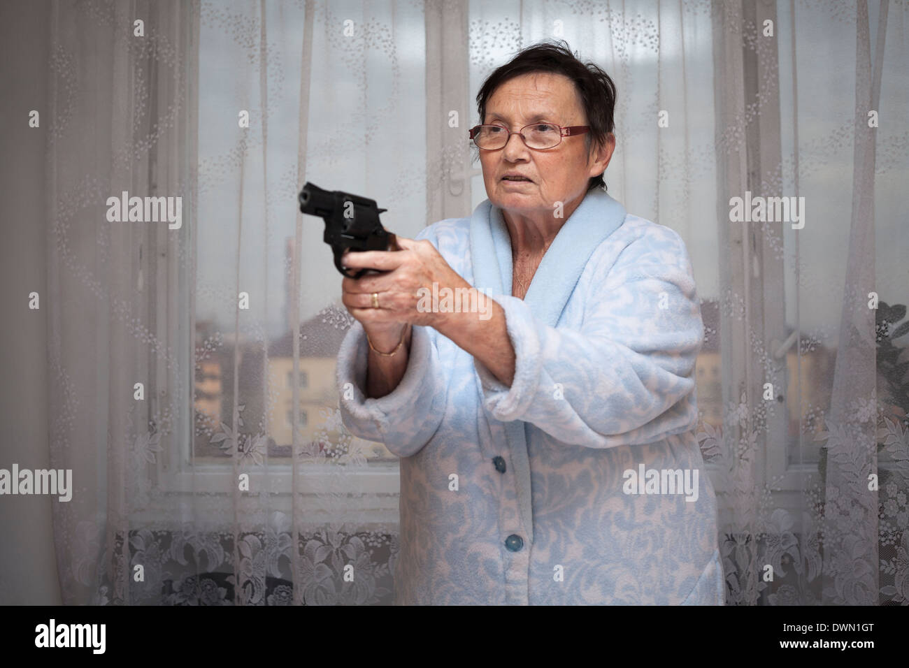 Spaventata senior donna puntando una pistola in ambienti chiusi. Foto Stock