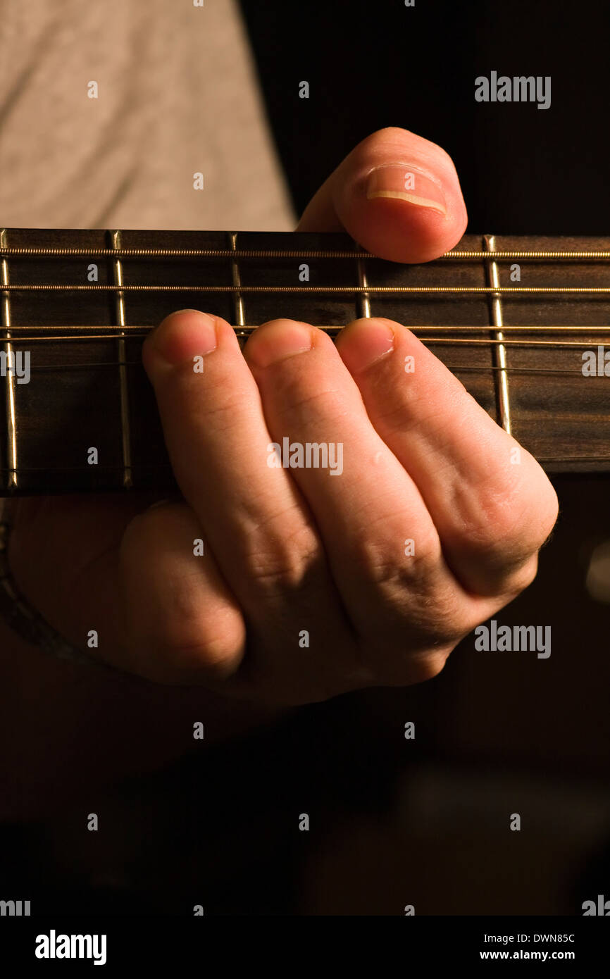 Un chitarrista la piegatura di una nota sul G stringa di una chitarra acustica con sfondo nero Foto Stock
