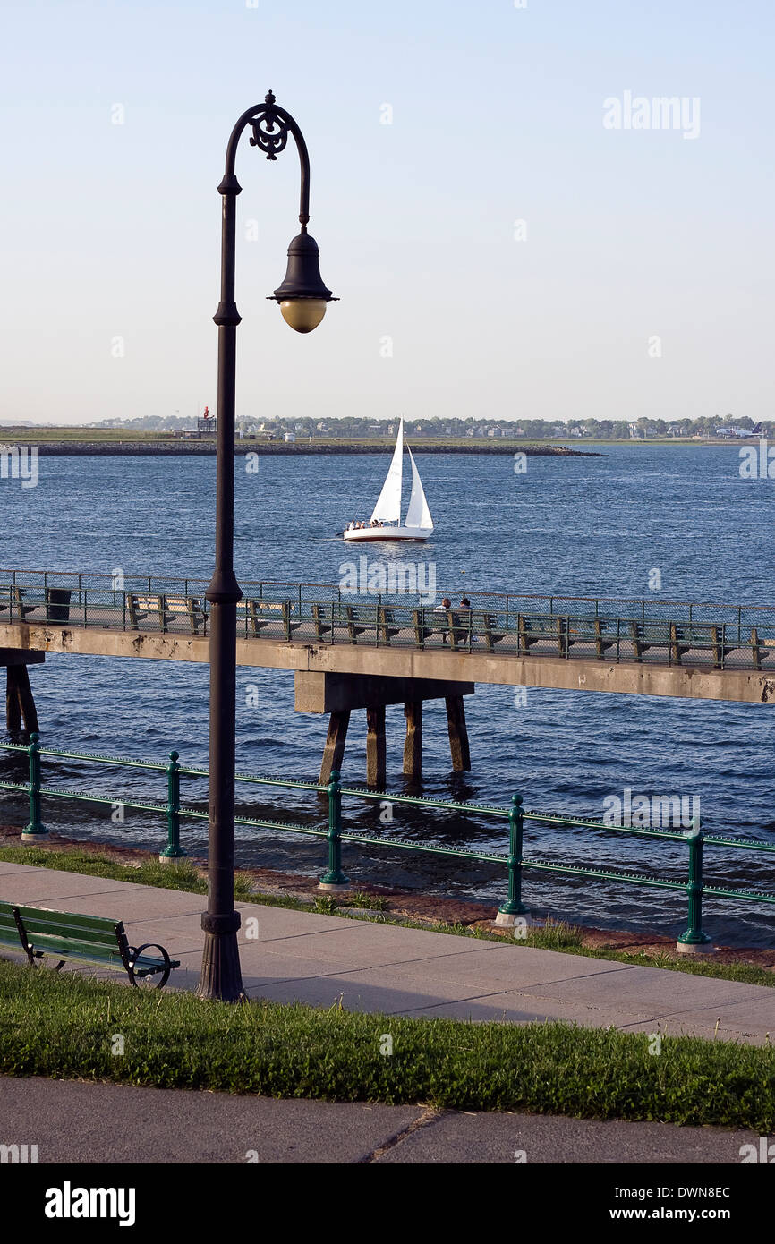 Lampione stradale di ornati e banco pubblico definisce il bordo di un percorso pedonale lungo la sponda del porto di Boston in massa di Boston Foto Stock