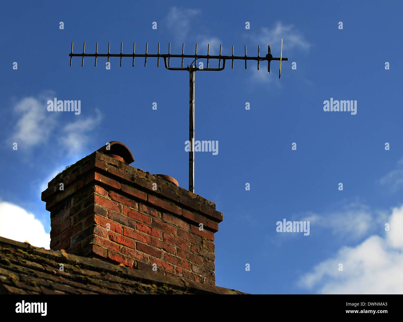 Antenna televisione attaccato ad una vecchia ciminiera in mattoni insieme contro un luminoso cielo blu su un cottage Foto Stock