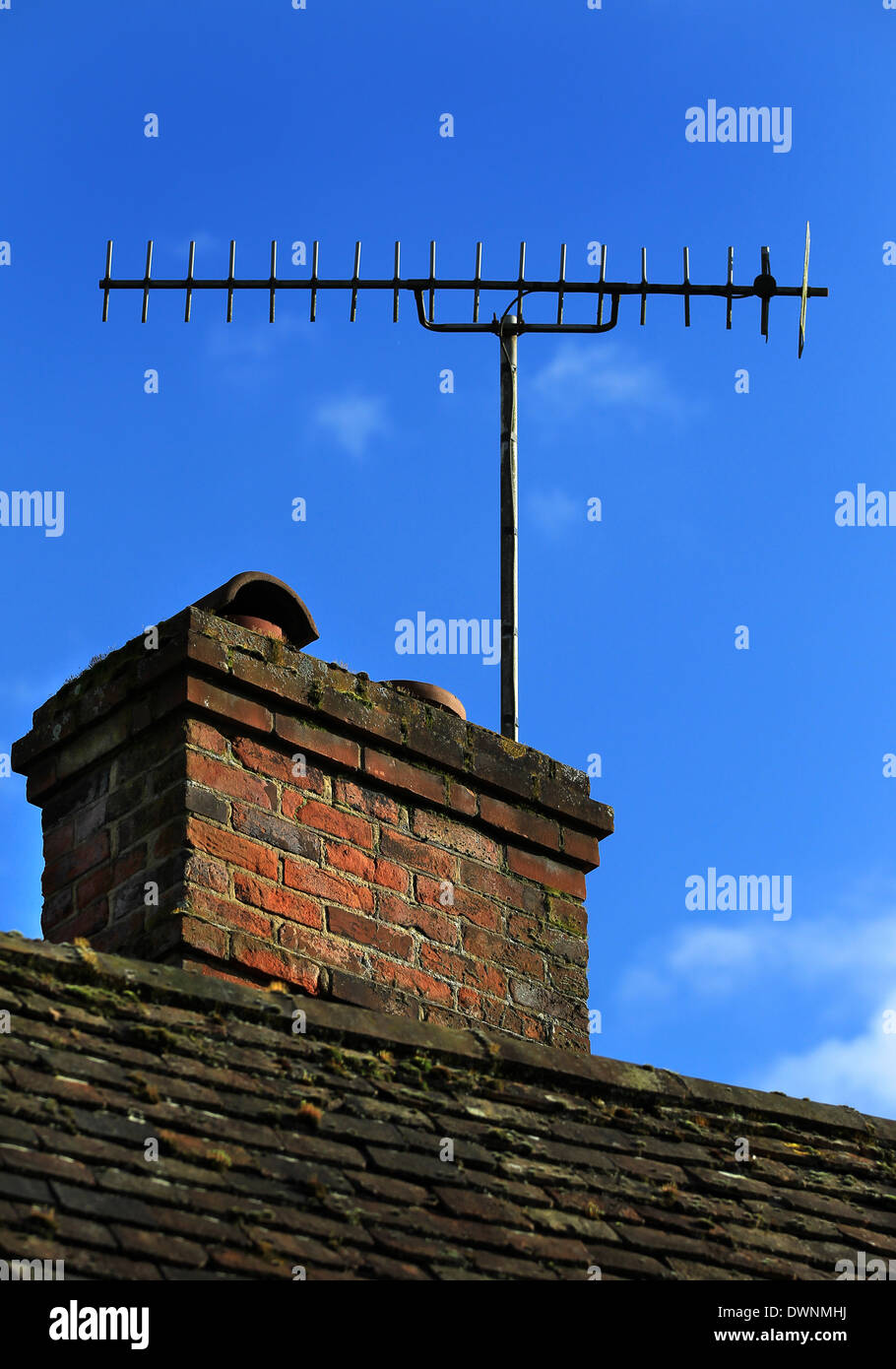 Antenna televisione attaccato ad una vecchia ciminiera in mattoni insieme contro un luminoso cielo blu su un cottage Foto Stock