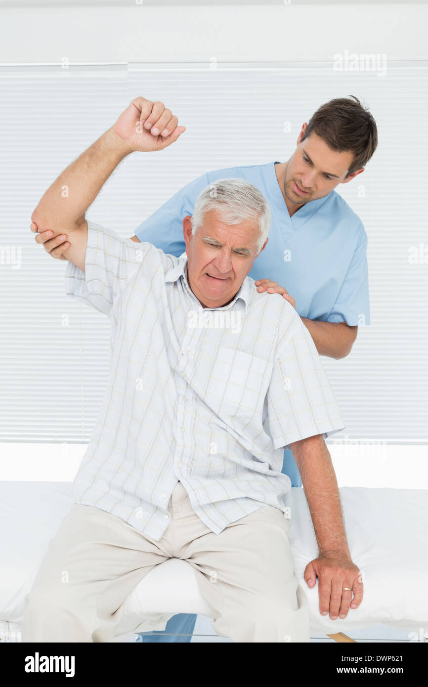 Mhysiotherapist assistere uomo senior di alzare la mano Foto Stock