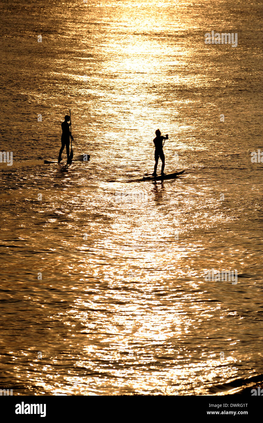 Brighton SUSSEX REGNO UNITO 12 Marzo 2014 - Paddle boarders catturare gli ultimi raggi di sole al tramonto dal Molo Ovest di Brighton dopo un altro bel calda giornata di primavera sulla costa sud dove le temperature raggiunte alte teens centigradi Foto Stock