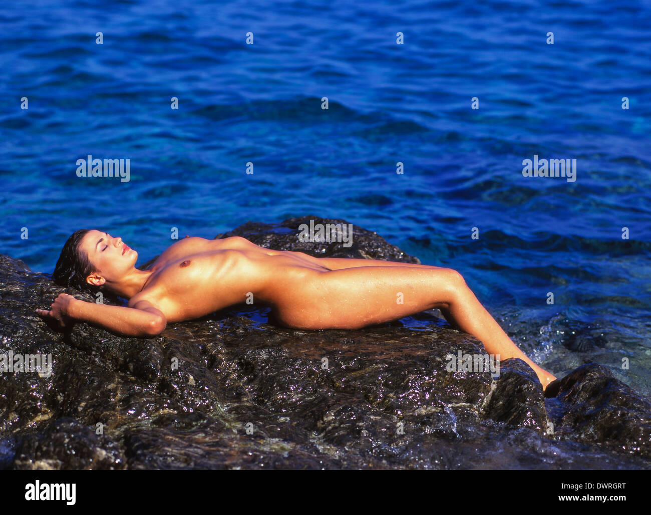 Giovane donna nuda ensoleillement stesso su una roccia sul mare, nudisti  naturista Foto stock - Alamy