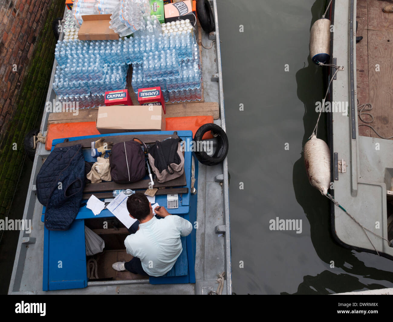 Un deliveryman nella sua barca da carico che offre cibo e bevande per ristoranti a un canale del centro storico di Venezia Foto Stock