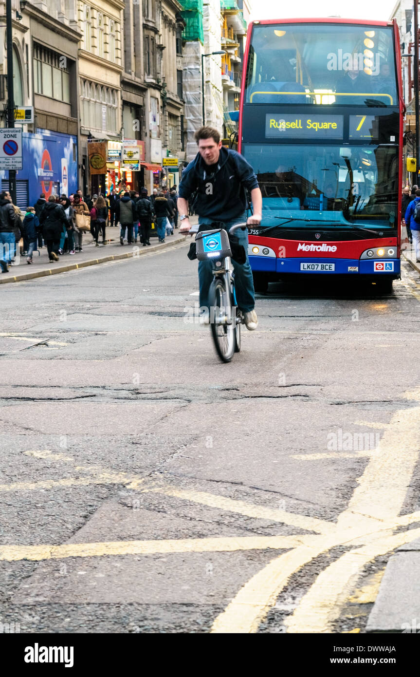 Ciclista utilizzando blu Barclay la bicicletta di andare in New Oxford Street passando dalla stazione di Tottenham Court Road Junction Foto Stock