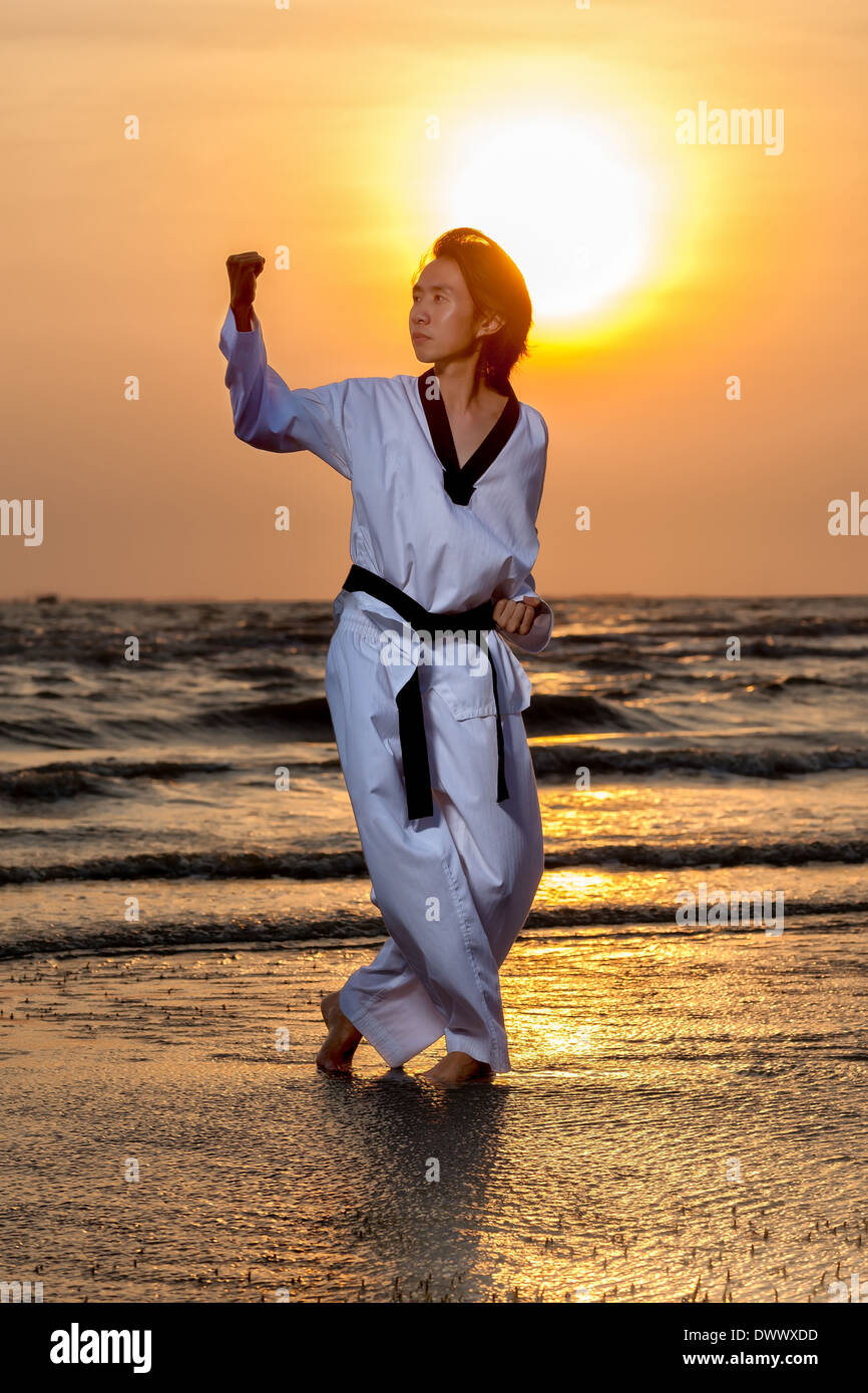 Arti marziali uomo formazione taekwondo sulla spiaggia al tramonto Foto Stock