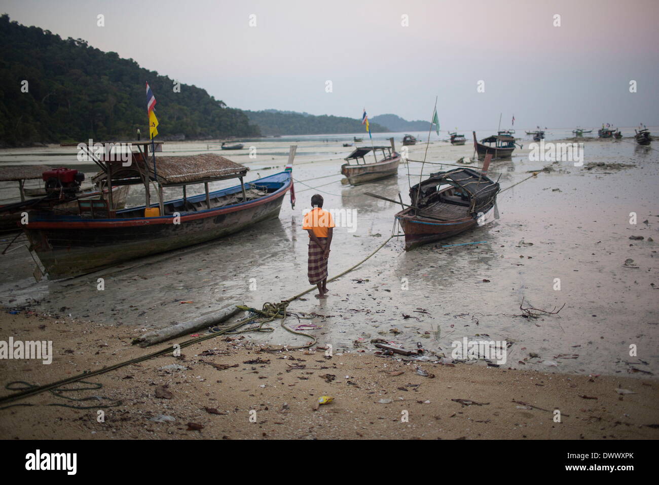 Mar 2, 2014 - Ko Surin, Tailandia - un anziano Moken uomo cammina verso la sua barca con la bassa marea. Spesso chiamata mare nomadi o zingari del mare, il Moken sono un popolo di mare che per secoli hanno vissuto nomadically sul Mare delle Andamane. Tuttavia, grazie a un più severo controllo di frontiera, commerciale sovrasfruttamento, rapido sviluppo e turismo, il Moken sono stati progressivamente costretti ad adottare uno stile di vita stanziale. Oggi il Moken che vivono in Koh Surin National Park, uno di Thailandia più remote del gruppo di isole, sono meglio di molti dei loro parenti e sono ancora in grado di vivere uno stile di vita basato in gran parte sulla tradizione e la se Foto Stock