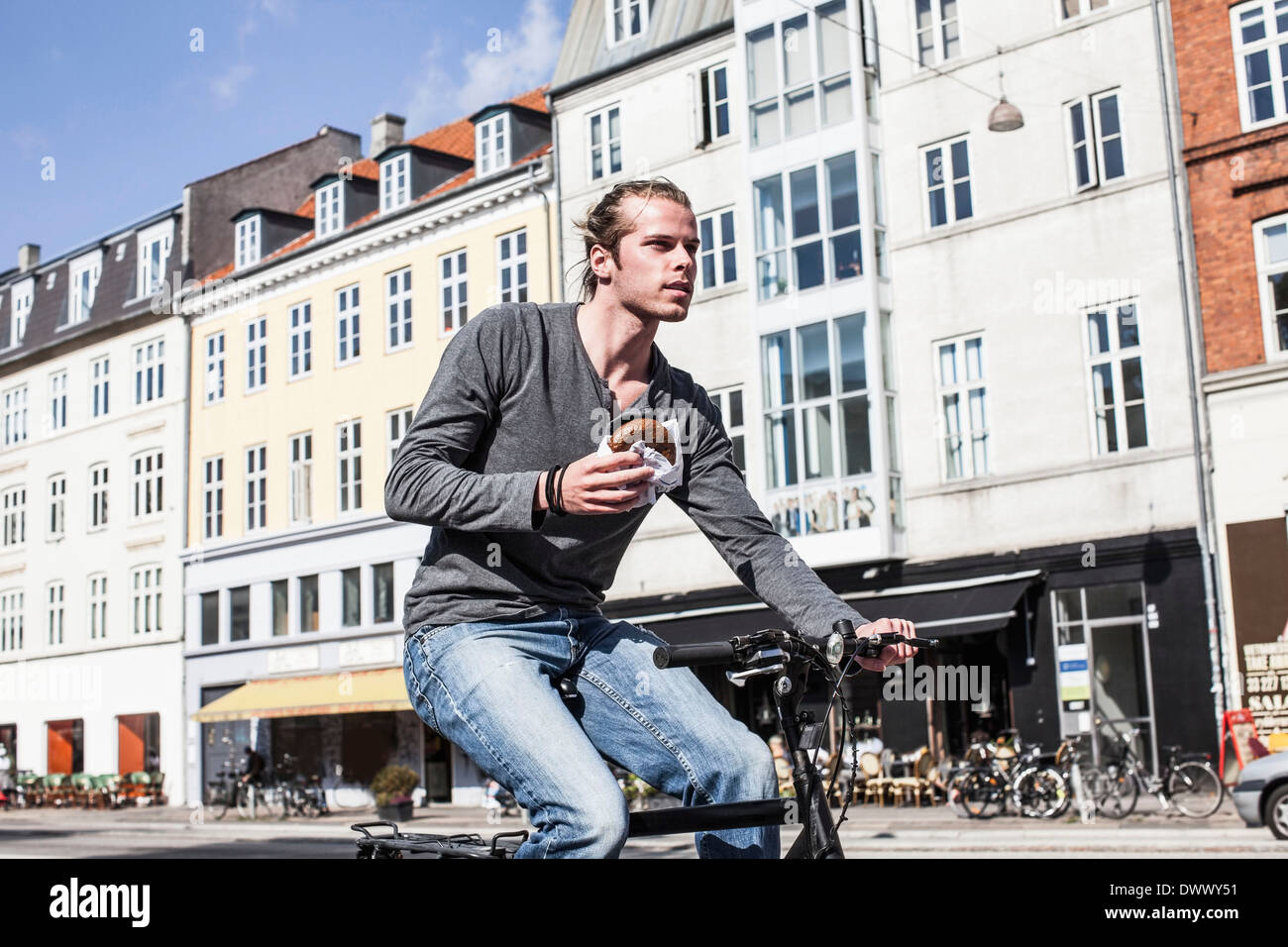 Giovane Azienda burger mentre equitazione Bicicletta su una strada di città Foto Stock